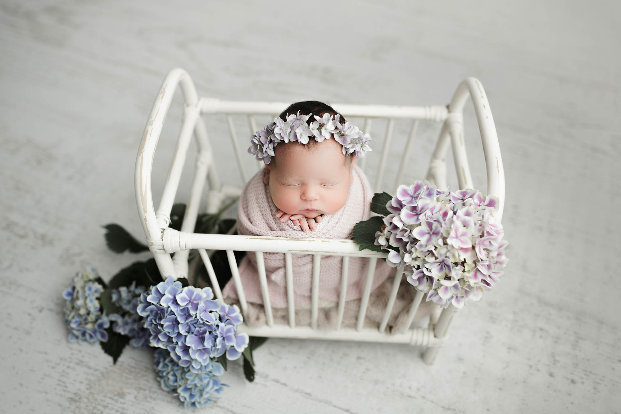 Saren Cassotto Canton Newborn Photographer photo of newborn baby girl in miniature crib with a floral crown and surrounded by flowers in potato sack pose