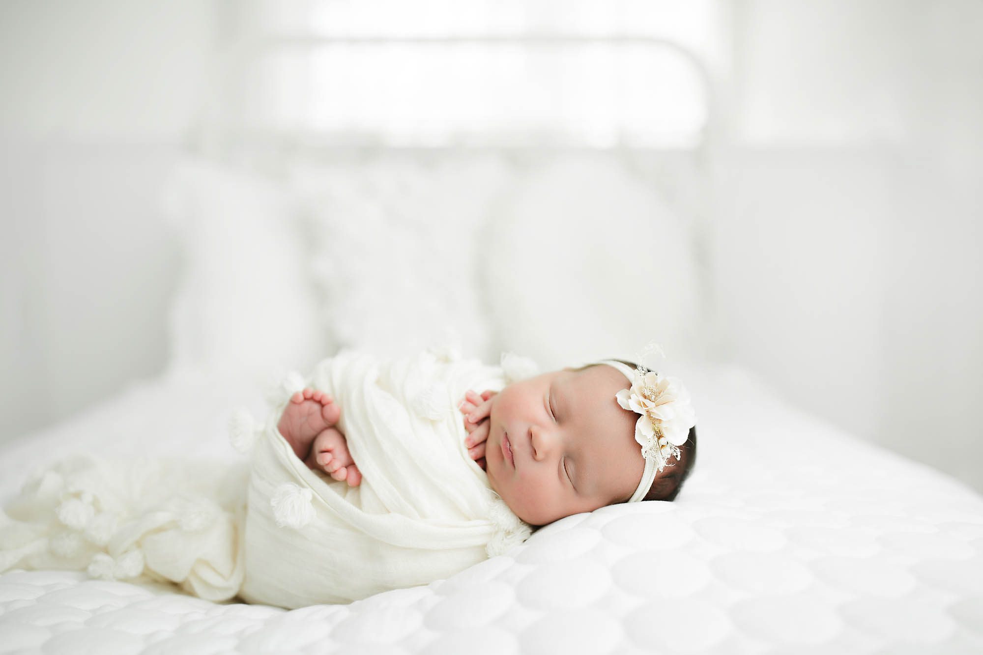 Newborn Girl wrapped in white with toes out of wrap laying on side against a white blanket wearing a white headband by Canton Newborn Photographer Saren Cassotto