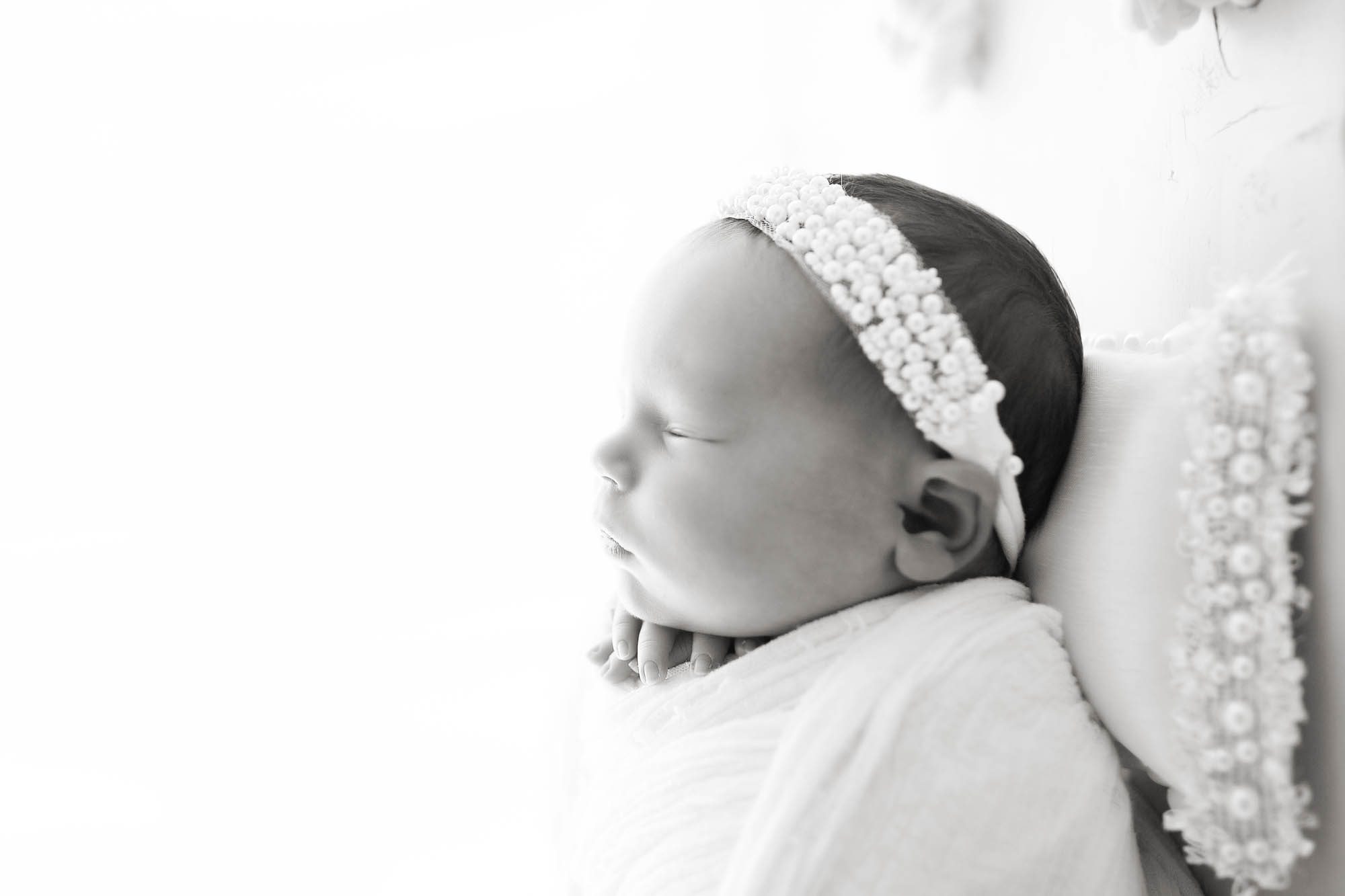 Black and white photo by Canton Newborn Photographer Saren Cassotto with baby girl in white wrap and white headband profile view