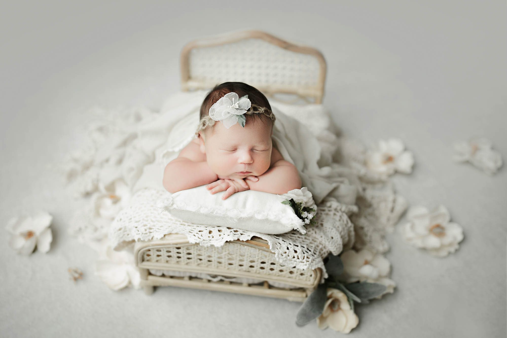 Canton Newborn Photographer newborn girl on miniature bed prop with head on hands and a white floral headband